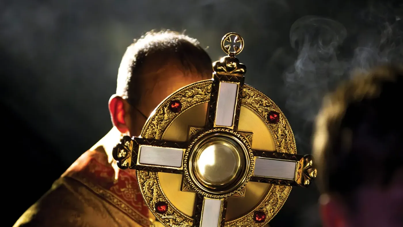 A priest in a gold cope raises the monstrance at Benediction as incense rises